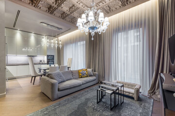A spacious living room features a cozy beige sofa and a stylish chandelier, showcasing a modern...