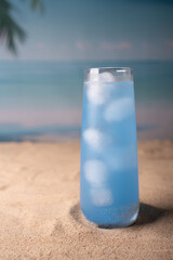 refreshing blue beverage in tall glass with ice cubes invokes serenity on sandy beach under tropical skies with palm leaves and ocean horizon in soft pastel colors, scenic, isle, clearwater