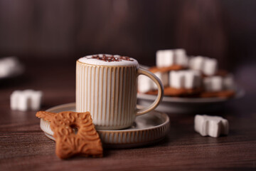 cozy coffee scene with foam-topped mug, crispy biscuit, and sugar cubes on rustic wooden surface evoking warmth and comfort in neutral tones, tactile, peaceful, elegant, aromatic, appetizing