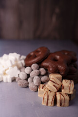 assortment of confections featuring chocolate-covered cookies, powdered sugar coated almonds, and cream drizzled cubes arranged on a muted surface with soft lighting, variety, mixture, complement