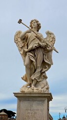 Rome, Italy - 12 January 2025. An angel sculpture with a sponge-tipped staff stands on Ponte Sant’Angelo, framed by a soft blue-grey sky.