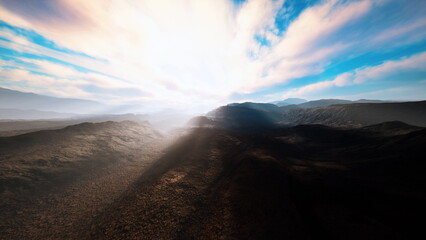 Soft rays of sunlight emerge from behind rugged mountains, casting long shadows across the rocky landscape. The brilliant sky melds colors as a new day begins, promising adventure.