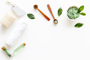 Spa pedicure accessories and organic cosmetics products - tea tree essential oil and sea salt near green leaves top view