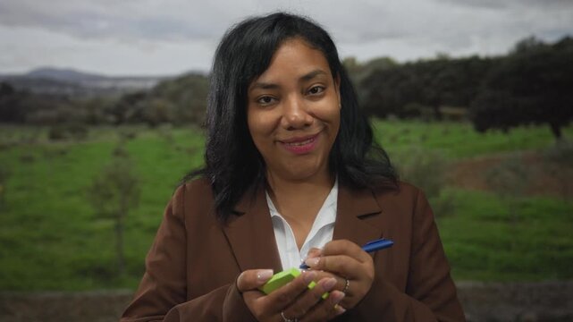 Woman writing with blue pen on green notepad in forest clearing with focused expression; concentration planning.