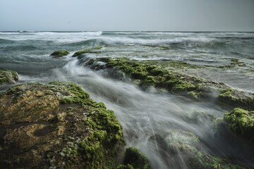 Ocean waves washing over moss-covered rocks creating serene coastal scenery photography with soft and airy feel