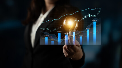 A businesswoman presents a light bulb symbolizing innovation against a backdrop of financial graphs. This image captures ideas for growth and strategies in the finance sector. Scalp