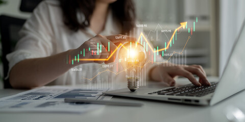 A business professional engages with financial data at a modern workspace, highlighting innovation and growth through dynamic visual elements and a light bulb symbol. Scalp
