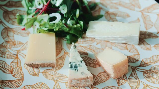 Close up of a cheese plate with assorted cheeses and salad on an elegant patterned plate