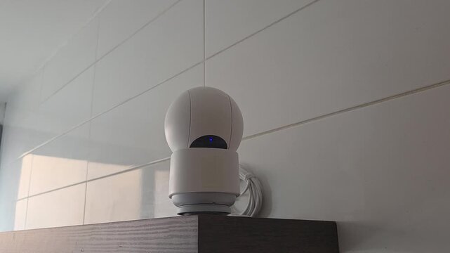 Smart home security camera blinking and scanning in modern interior setting with tiles reflection. Home indoor security camera - turns off privacy mode and opens the lens