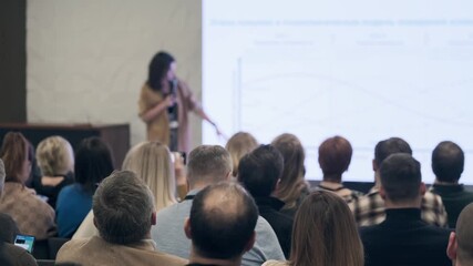 Audience focuses on presenter in conference room as slides illuminate screen and convey information