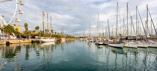 Great panoramic view of the port of Barcelona with a Ferris wheel and many sailing boats docked in the port, Spain.