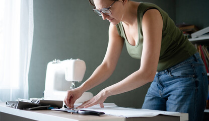 Female seamstress using a chalk to mark a sewing pattern on the textile material at her workshop table before cutting.