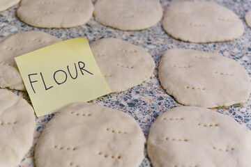 Raw dough circles, meticulously arranged and prepped for baking, with the word Flour scribbled on a sticky note. Capturing the essence of a homely baking, food preparation scene.