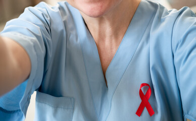 Female medical professional in uniform taking smartphone selfie with red awareness ribbon, showing solidarity with HIV AIDS patients and support.