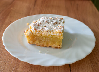 A square slice of apple crumb cake sits on a white plate, topped with powdered sugar. Soft textures and warm tones create a cozy homemade dessert scene perfect for bakery, recipe, and comfort food the