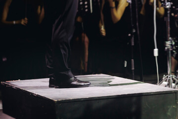 Male conductor behind the podium directing orchestra on stage with pupitre, musicians and choir, the philharmonic venue hall during concert, symphony orchestra director hands conducting waving baton