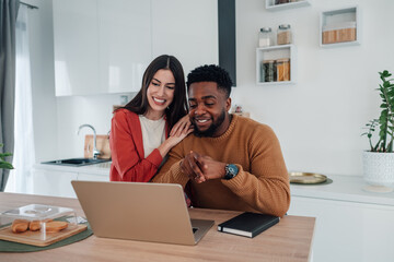 Happy diverse couple browsing laptop together at home