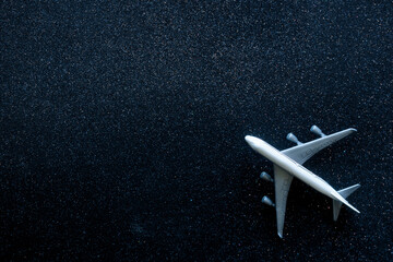 Top view of a white toy airplane on a black glitter background resembling a starry night sky. Concept of air travel and tourism with copy space. Photo