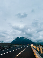Fototapeta premium Winding highway stretching through mountain valley under cloudy sky during tranquil evening, evoking serene and peaceful atmosphere perfect for reflection and exploration. Scenic mountain backdrop