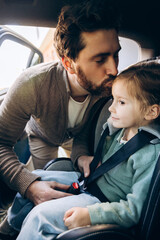Handsome father putting daughter in car seat and kissing her