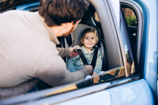 Father buckling child, cute little girl into car seat for safety