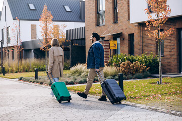 Happy couple walking with suitcases leaving home for travel outdoors