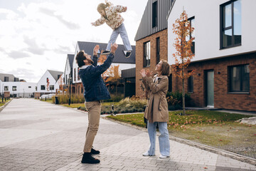 Cheerful family playing with child outdoors in modern suburban neighborhood