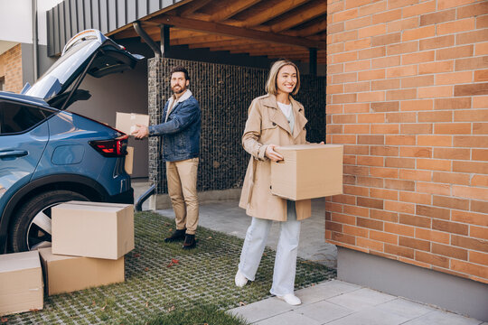 Smiling, happy couple, cheerful woman and man moving home, unpacking boxes from car - Powered by Adobe