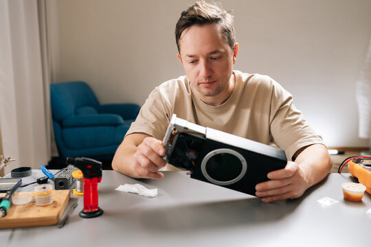 Thoughtful technician male completing electronic repairs in professional workshop, holding disassembled hardware, exposing intricate internal components and ensuring proper functionality.