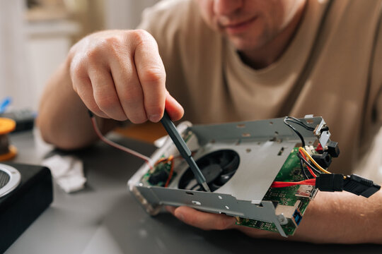 Close-up cropped shot of technician working on electronic device, holding computer hardware with exposed cooling fan, performing repairs and maintenance on tech equipment in modern workshop.