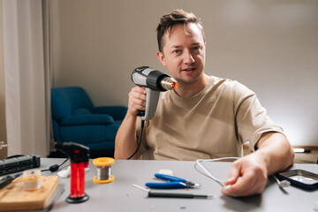 Professional repairman working on damaged electronic cable, applying heat with heat gun to shrink tubing or solder connecting wires, signifying diligent repair work and technical expertise.