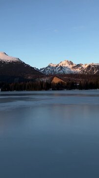 Strbske pleso, High Tatras, Slovakia. Winter ladscape of frozen mountain lake and hills and mountains covered by snow. Evening and sunset. Vertical panning video.