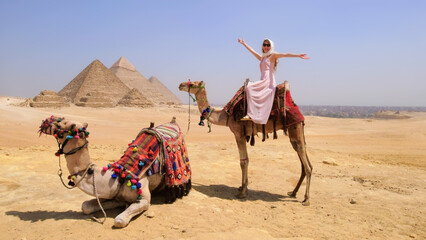 A joyful traveler rides a camel in the Egyptian desert with the iconic Giza pyramids in the background, capturing the perfect vacation moment.
