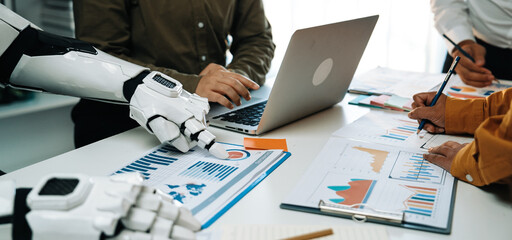 A dynamic meeting scene featuring a robot arm assisting in data analysis, showcasing teamwork and innovation in a modern office environment focused on productivity.Noogenesis