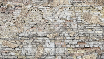 Textured background of an old, weathered brick wall with patches of rough, crumbling plaster