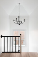 A hallway and staircase with a wrought iron railing, hardwood floor, and chandelier hanging from...