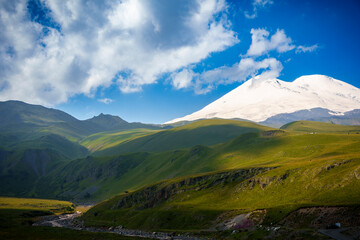 Mount Elbrus with snow-covered peak and green hills in foreground