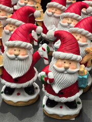 A close-up view of numerous ceramic Santa Claus figures standing in a group. They wear red hats and hold candy canes, creating a dense, repetitive Christmas decoration display.