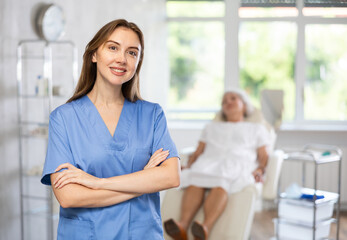 Fototapeta premium Portrait of young female doctor in scrub standing while senior patient laying in the back.