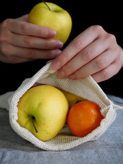Hand Putting Apple Into Reusable Cotton Mesh Bag With Tangerines and Apples - Eco Friendly Zero Waste Grocery Concept