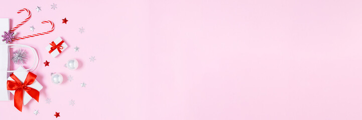 Christmas gifts, candy canes and festive ornaments in white paper bag on pastel pink background with wide copy space for holiday banners, ads and seasonal design layouts. Flat lay