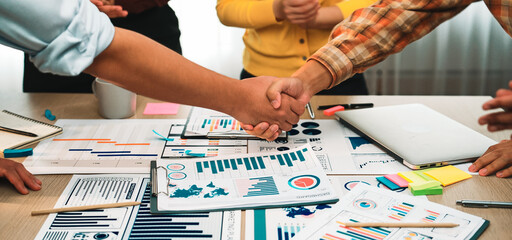 A dynamic scene showing hands shaking over various business documents, charts, and reports on a table, symbolizing collaboration and partnership in a professional setting. SACTR