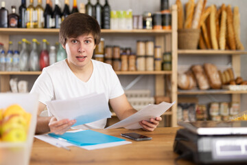 Young manager of a grocery supermarket keeps count of goods and makes entries in a journal