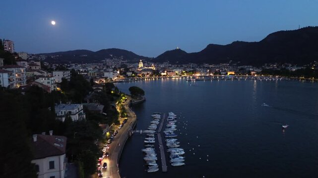cinematic nocturnal aerial drone view of dazzling lights over Lake Como with motorboats leaving white trails on the blue waters