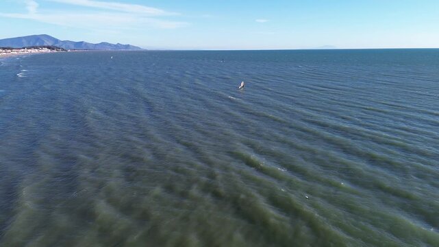 Cinematic aerial view of windsurfers performing acrobatics on a windy winter day along the blue Italian coast