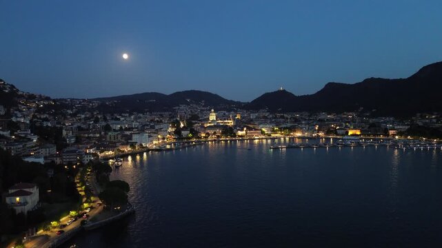 cinematic nocturnal aerial drone view of dazzling lights over Lake Como with motorboats leaving white trails on the blue waters 2
