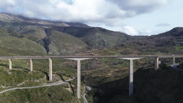 Aerial view of a modern viaduct with winter green mountains and cloudy blue sky in the background