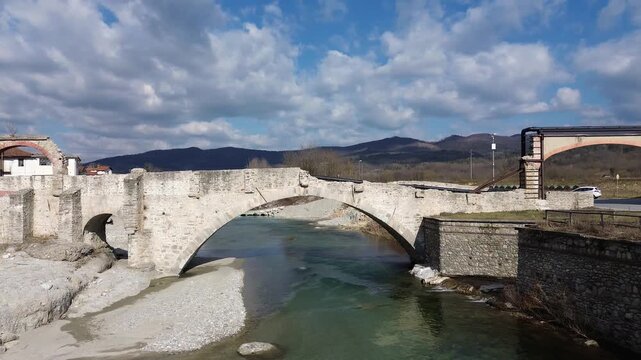 Aerial drone footage of a serene river winding through the lush springtime plains of Piedmont near Cuneo province with warm sunlight illuminating the rural Italian countryside and rolling green meadow