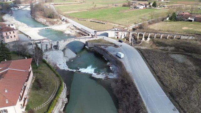 Aerial drone footage of a serene river winding through the lush springtime plains of Piedmont near Cuneo province with warm sunlight illuminating the rural Italian countryside and rolling green meadow