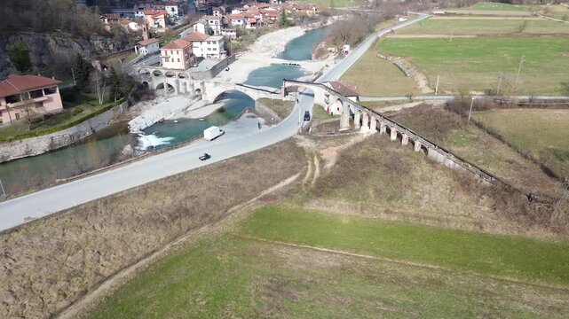 Aerial drone footage of a serene river winding through the lush springtime plains of Piedmont near Cuneo province with warm sunlight illuminating the rural Italian countryside and rolling green meadow